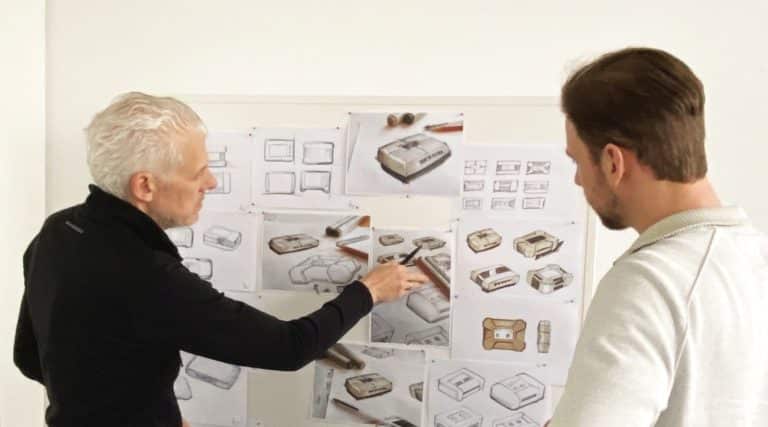 A man with a creative car design, making a gesture and wearing glasses. The image shows art, engineering and technology as well as a font at an event related to the job.