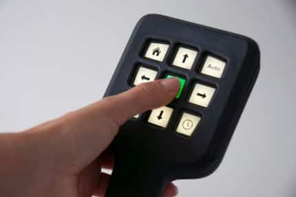 "Person points with thumb to a gadget with a numeric keypad and display surrounded by fonts and numbers on a rectangular display on the wrist."