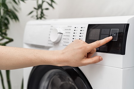 Hand drückt auf Bedienpanel einer Waschmaschine