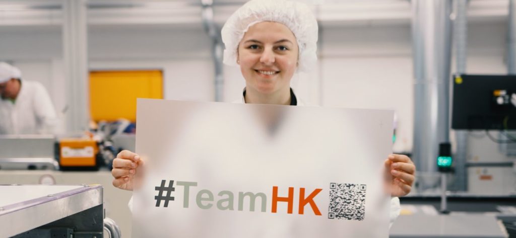 Hoffmann + Krippner - Employee lifts printed film with #TeamHK into the camera